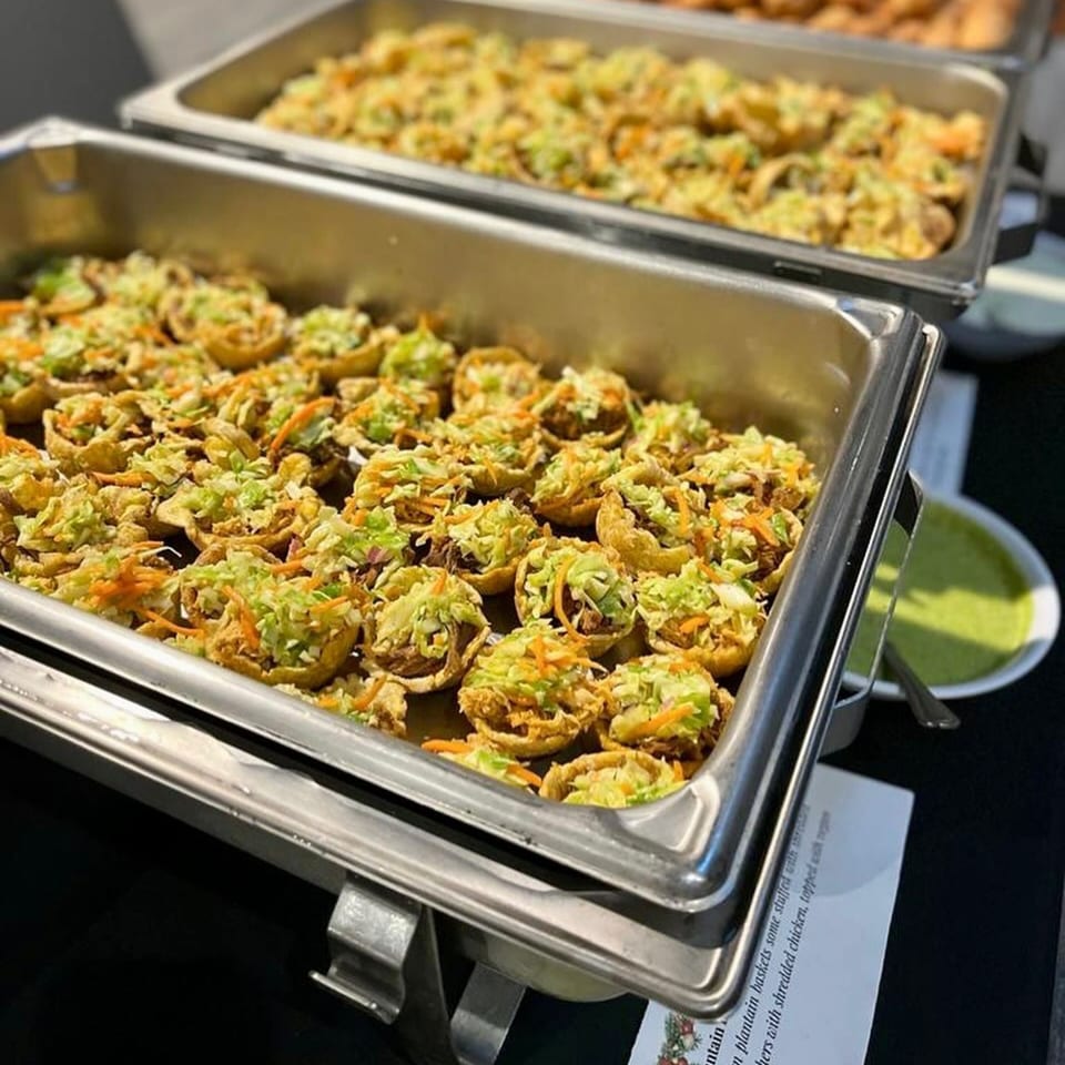 Two chafing dishes filled with Venezuelan plantain baskets topped with shredded chicken and slaw.