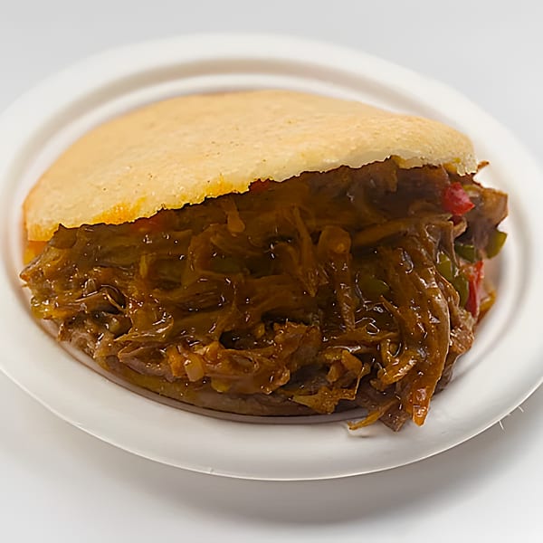 A Venezuelan La Arepa with shredded beef and vegetables on a white plate.
