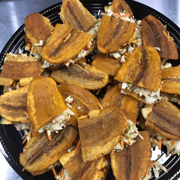 A platter of golden-brown plantain sandwiches filled with coleslaw, cheese, and sauce.
