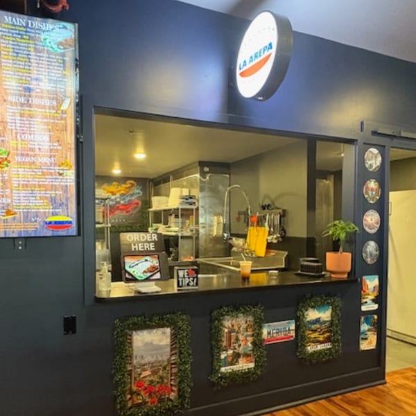A restaurant counter with an "Order Here" sign, a menu board, and a La Arepa sign.