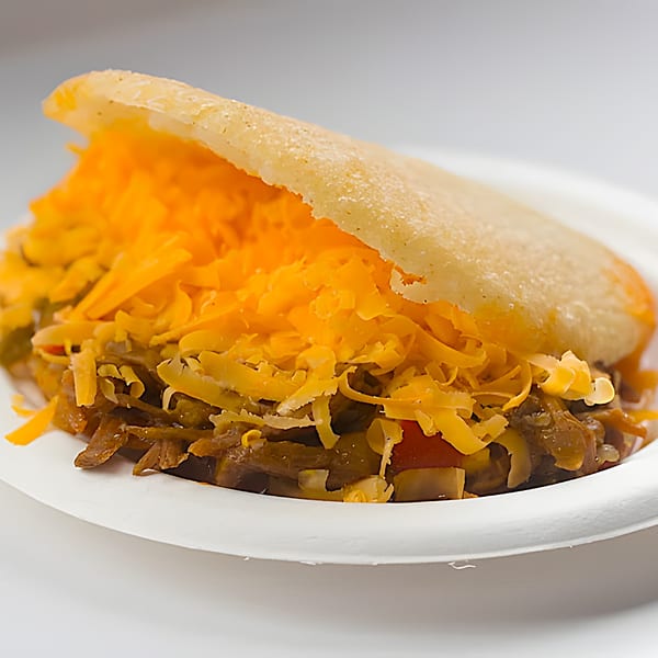 A Venezuelan La Arepa with shredded beef and bright orange shredded cheese on a white plate.