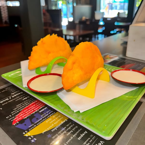Two golden-fried Venezuelan empanadas with dipping sauces on a green platter at La Arepa.