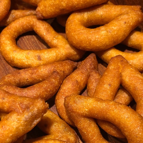 Close-up of golden-brown, ring-shaped Venezuelan churros, glistening with sugar, on a wooden surface.