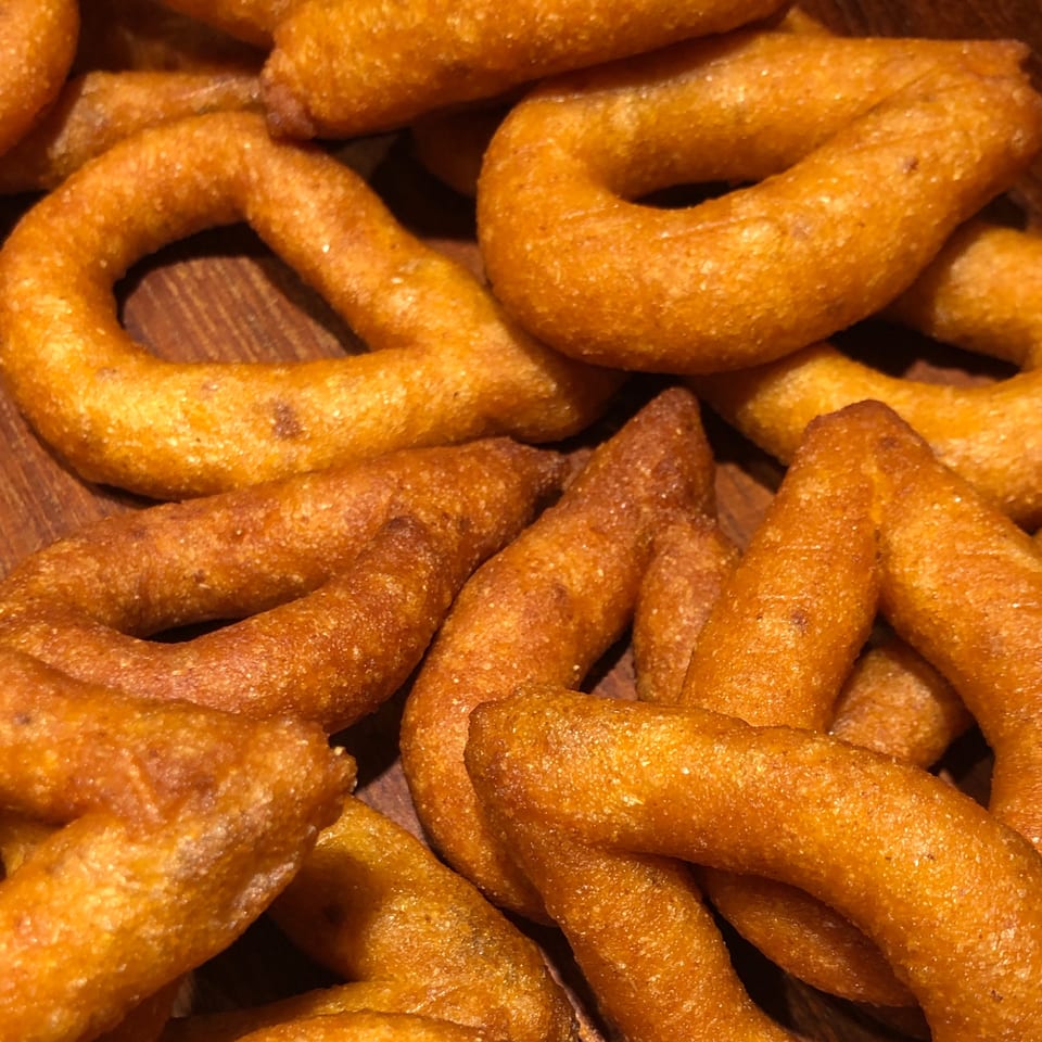 Close-up of golden-brown, ring-shaped Venezuelan churros, glistening with sugar, on a wooden surface.