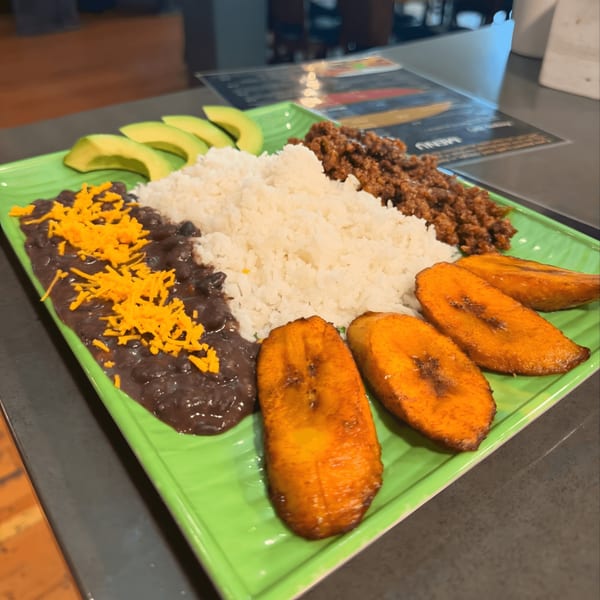 Venezuelan pabellón criollo with rice, black beans, shredded beef, plantains, and avocado on a green plate.