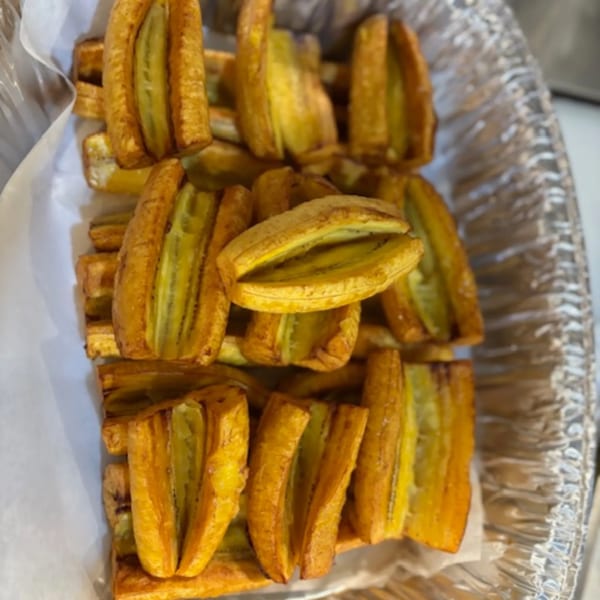 Golden-brown fried plantains, split lengthwise, arranged in a foil container lined with white paper.