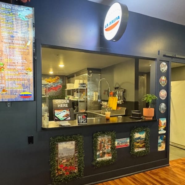 La Arepa restaurant interior with a service window, menu board, and decorative wall art.