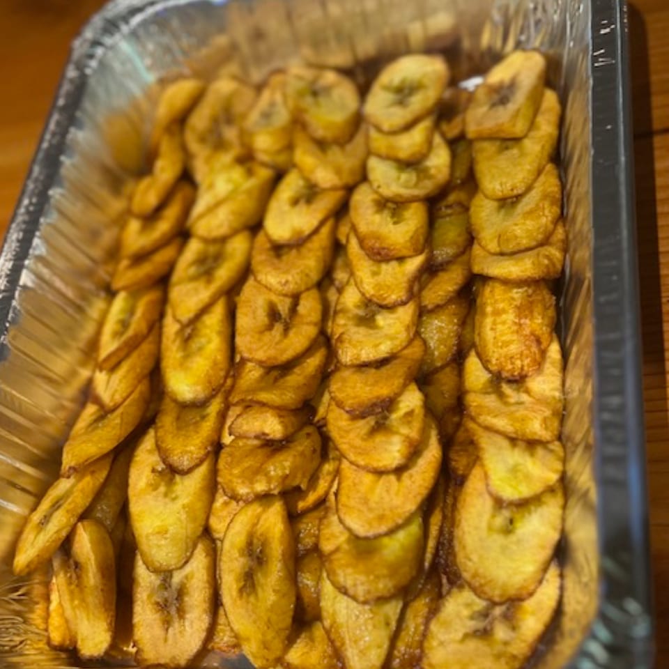 Close-up of golden fried plantain slices, known as tajadas, in a foil tray from La Arepa.