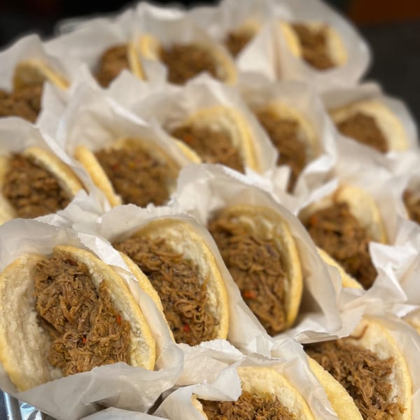 Rows of La Arepa's Venezuelan shredded beef arepas, each wrapped in white paper.