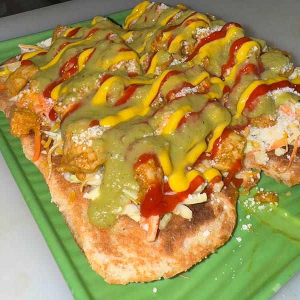 Venezuelan arepa topped with chicken, shredded cabbage, cheese, ketchup, mustard, and green sauce on a green plate.