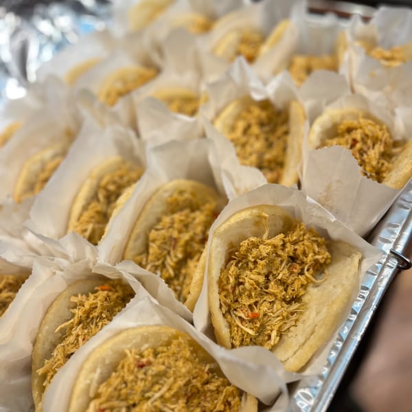 Numerous Venezuelan La Arepa chicken arepas, wrapped in paper, are arranged in a foil tray.