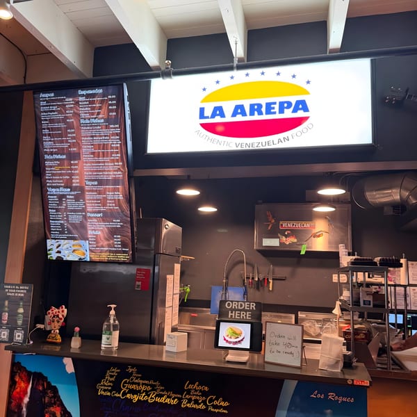 A wide shot of La Arepa's counter, menu boards, and kitchen area with a prominent "ORDER HERE" sign.