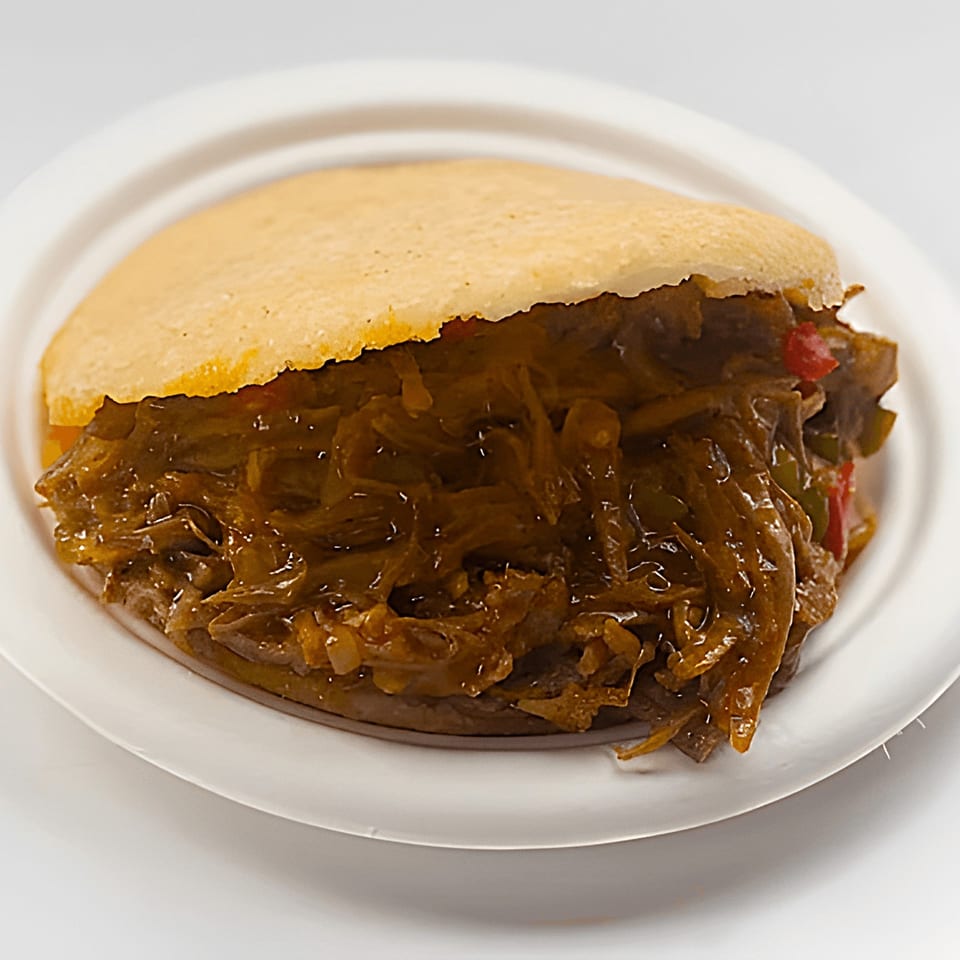La Arepa's Venezuelan shredded beef and vegetable-filled arepa on a white plate.