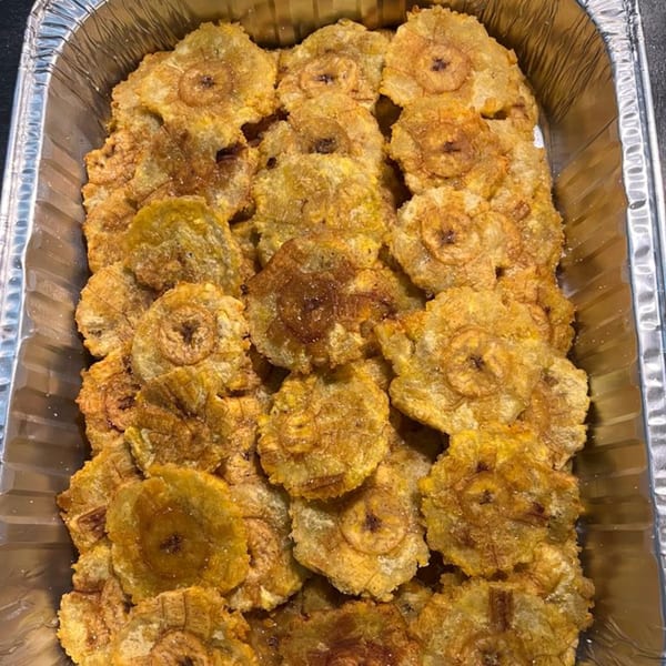 Close-up of golden-brown tostones, or fried plantain slices, in a silver foil tray at La Arepa.